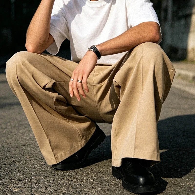 Seated man wearing khaki pleated wide straight-leg trousers