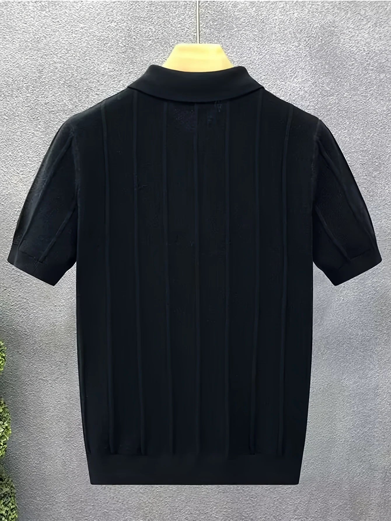 Back view of a black textured knit polo on a hanger